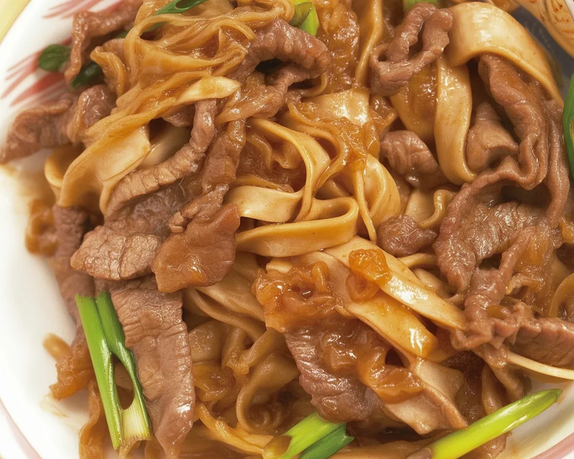 A delicious plate of Beef Chow Fun with tender beef and flat rice noodles served hot.